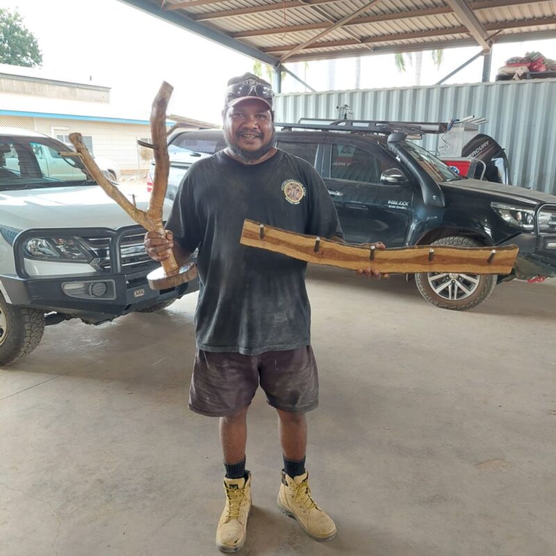 First Nations man holds two items built from local bush timber to hone carpentry skills