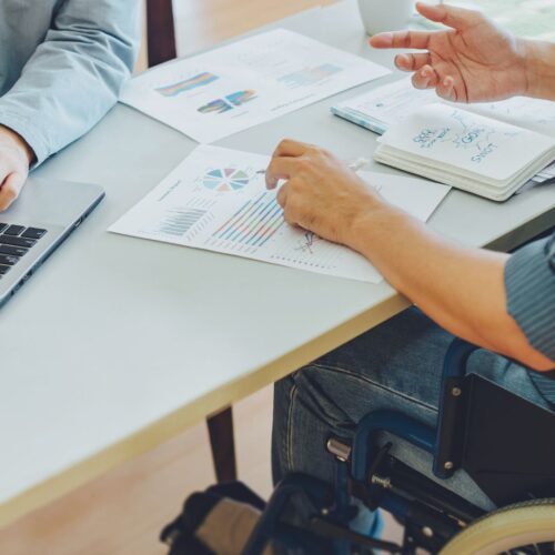 A person with disability sits at a desk working on goals and career aspirations with another person.